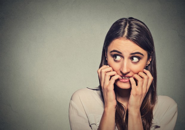 Closeup portrait young unsure hesitant nervous woman biting her fingernails craving for something or anxious, isolated on gray wall background. Negative human emotions facial expression feeling