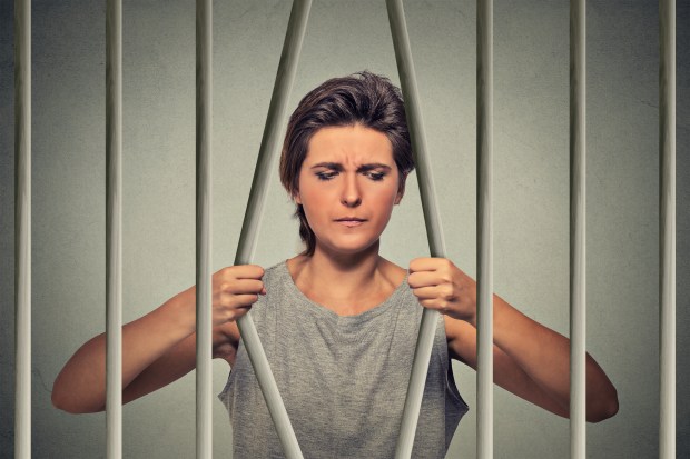 Stressed desperate sad woman bending bars of her prison cell isolated on grey wall background. Life limitations, law violation consequences concept. Face expression emotion