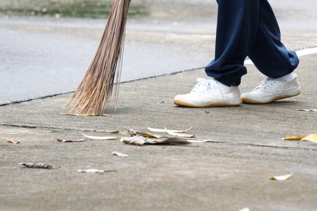 Student sweeping dried leafs on the floor in school.